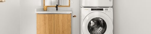 A white washing machine is in a laundry room with a mirror and wooden cabinets.