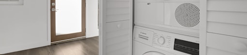 A white washing machine is placed next to a white wall.