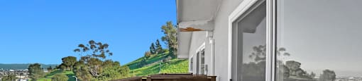 A balcony with a glass door overlooking a green landscape.