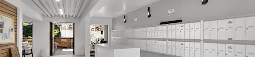 A white reception desk is in the middle of a hallway with white lockers on the wall.