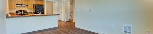 A spacious room with wooden flooring and a kitchen area with white countertops.