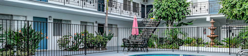 A swimming pool is surrounded by a black fence and a building with balconies.