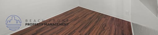 A room with wooden flooring and a logo for Beach Front Property Management on the wall.