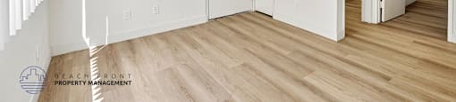 A white room with wooden floors and a logo for Beachfront Property Management in the bottom left corner.