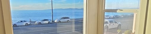 A room with two windows overlooking a parking lot and the ocean.
