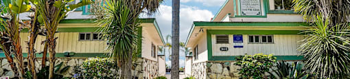 A green building with a sign on it and a tree in front.