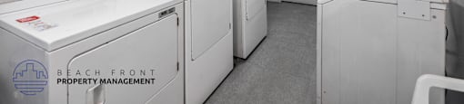 A clean, white-walled laundry room with washers and dryers.