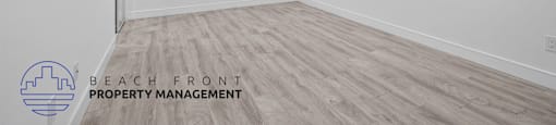 A spacious room with wooden flooring and white walls, managed by Beach Front Property Management.