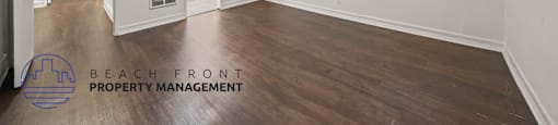 A spacious room with wooden floors and white walls, managed by Beach Front Property Management.
