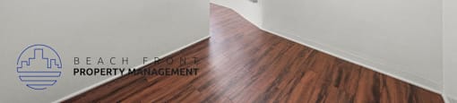 A room with wooden floors and white walls, with a logo for Beachfront Property Management on the wall.