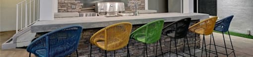 a bar with colorful chairs in front of a kitchen with a television