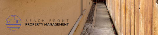 the side of a building with a sidewalk and a wooden fence