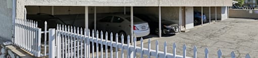 A white fence is in front of a building with cars parked in the garage.