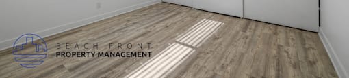 A room with a window and wooden flooring, with a logo for Beach Front Property Management.