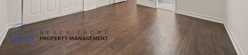 A room with wooden floors and white walls, with a logo for Beach Front Property Management in the bottom left corner.