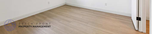 A room with a window and wooden flooring, managed by Beach Front Property Management.