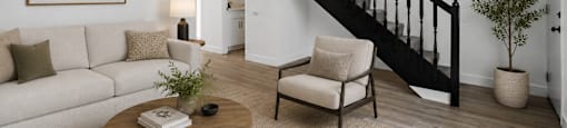 A living room with a white couch, a wooden coffee table, a chair, a potted plant, and a painting on the wall.