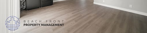 A spacious room with wooden flooring and a logo for Beach Front Property Management.