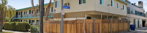 A building with a blue sign on the front is surrounded by a wooden fence.