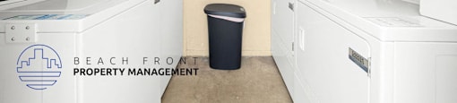 A room with a couple of washing machines and a trash can.