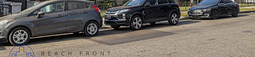 Three cars are parked in front of a building with the logo "BEACH FRONT PROPERTY MANAGEMENT" on the ground.