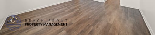 A room with wooden floors and white walls, with a logo for Beach Front Property Management in the bottom left corner.