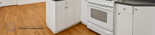 A kitchen with white cabinets and appliances, and a wooden floor.