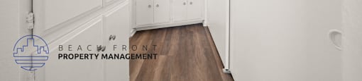 A hallway with white walls and a wooden floor leads to a bathroom.
