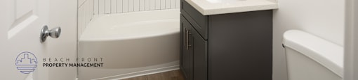 A white tiled bathroom with a sink, bathtub, and toilet.