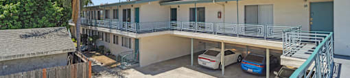 A sunny day at the apartment complex with cars parked in the driveway.