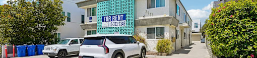 A white car is parked in front of a building with a for rent sign.