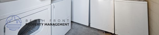 A laundry room with washers and dryers and a sign that says "BEACH FRONT PROPERTY MANAGEMENT".