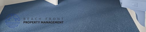 A room with blue carpet and white walls, with a logo for Beach Front Property Management in the bottom left corner.