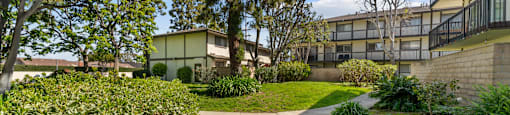 A concrete walkway leads through a landscaped area with a building in the background.