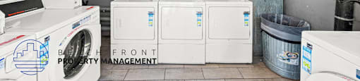 A laundry room with a washer and dryer, a fan, and a trash can.