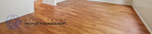 A spacious room with wooden flooring and a logo for Beach Front Property Management in the bottom left corner.