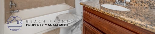 A bathroom with a beige tiled shower, a white toilet, a sink with a granite countertop, and a mirror above the sink.
