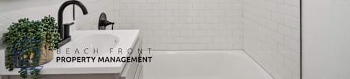 A white tiled bathroom with a large mirror and a plant on the sink.