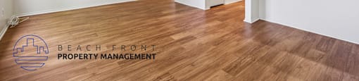 A room with wooden floors and white walls, with a logo for Beach Front Property Management in the bottom left corner.