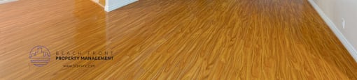 A spacious room with wooden flooring and a kitchen area in the background.