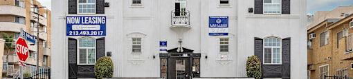 A white house with a black fence and a sign that says "NOW LEASING".
