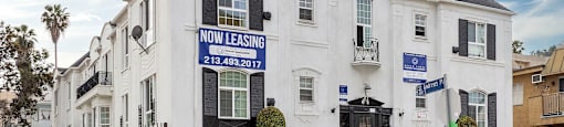 A white building with a black roof and a sign that says "NOW LEASING" is for property management.