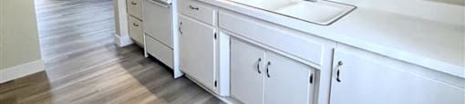 A kitchen with white cabinets and a wooden floor.