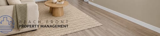 A living room with a couch, coffee table, and a rug with the logo of Beach Front Property Management.