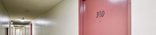 A hallway with a red door numbered 310.