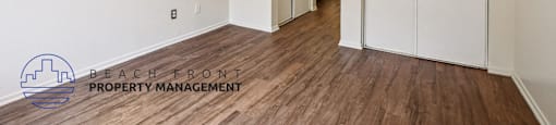 A room with wooden floors and white walls, with a logo for Beach Front Property Management in the bottom left corner.
