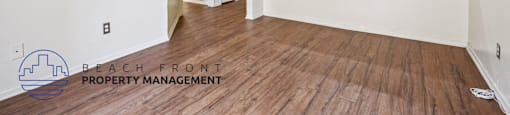 A room with wooden floors and white walls, with a logo for Beach Front Property Management in the bottom left corner.