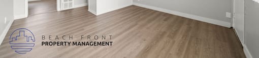 A room with wooden floors and white walls, with a logo for Beach Front Property Management in the bottom left corner.