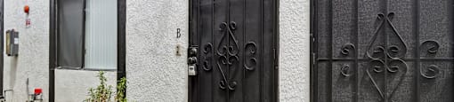 A black gate with a decorative design is on the right side of a white building.