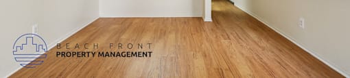 A room with wooden floors and white walls, with a logo for Beach Front Property Management in the bottom left corner.